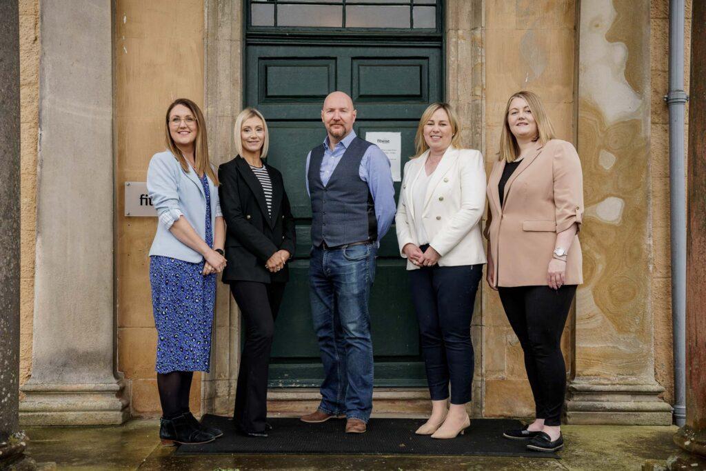 A photo of the Fitwise Senior Management Team standing in front of Blackburn House
